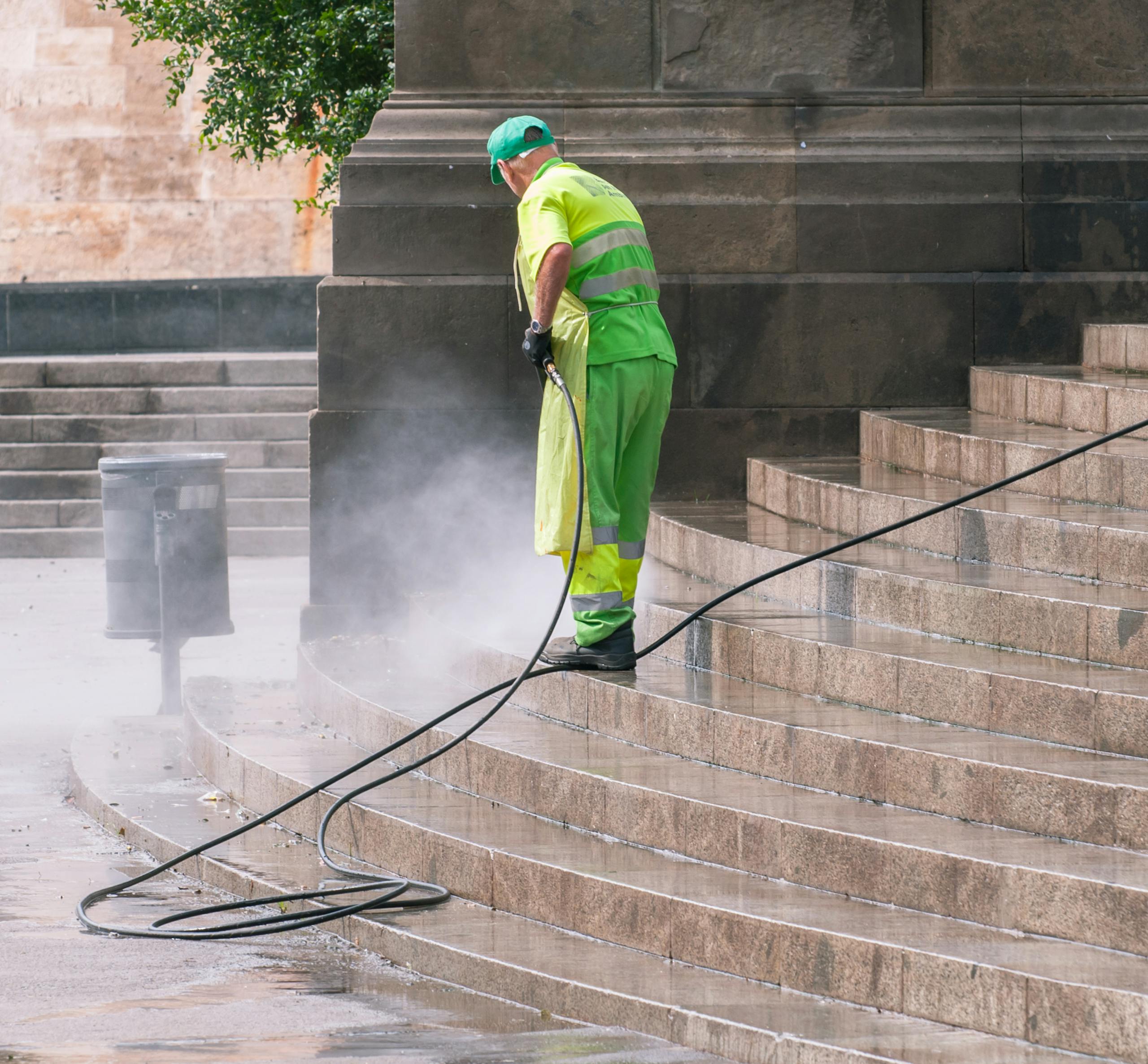 A street worker pressure washes stone stairs in a public park, ensuring cleanliness and safety.