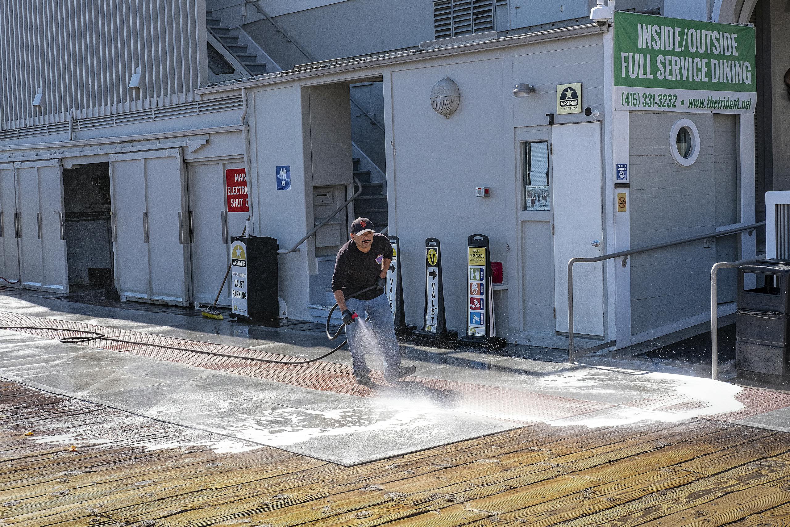 A worker uses a pressure washer to clean a sidewalk outside a dining facility.